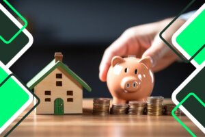 una mano que sostiene una hucha con varias monedas en el anverso y una casita de madera en miniatura al lado