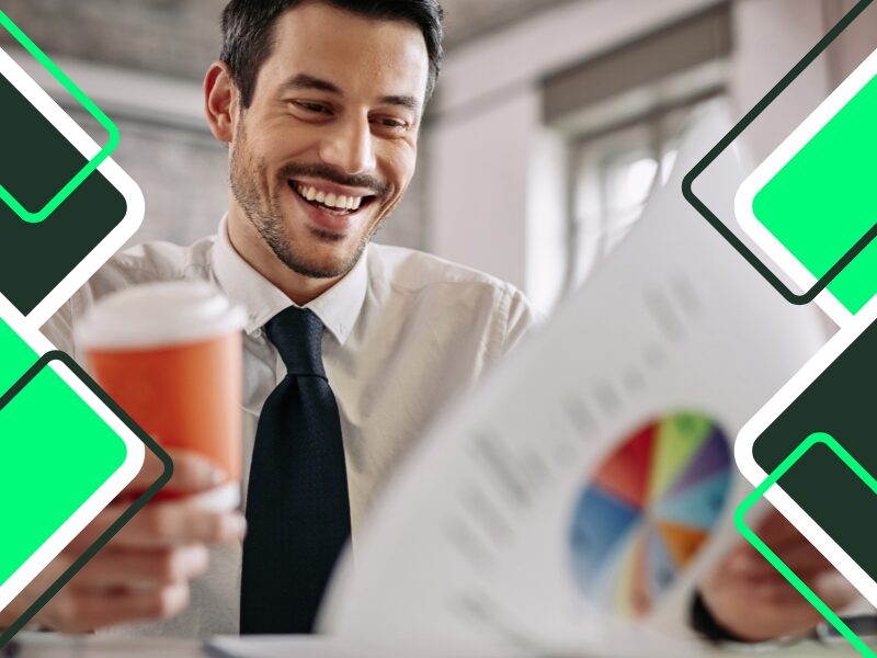 reduce your business costs: happy-young-manager-examining-business-progress-while-reading-charts-and-drinking-coffee-in-office
